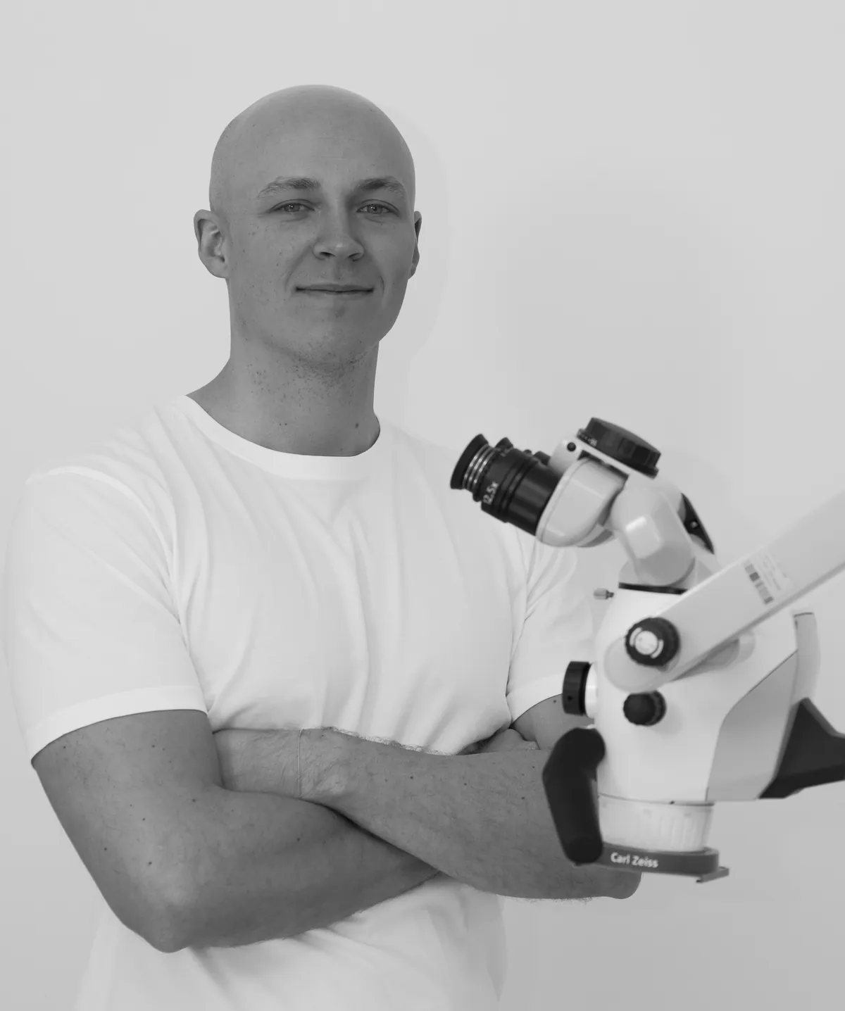 Dr. Philipp Brenner mit verschränkten Armen neben dem Operationsmikroskop